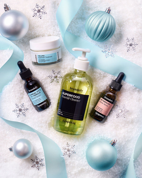 The four Defend Luxe Essentials products &mdash; cleanser, ceramide treatment, vitamin C serum and niacinamide serum &mdash; on fresh snow with pale blue ribbon, matte baubles and silver snowflakes.