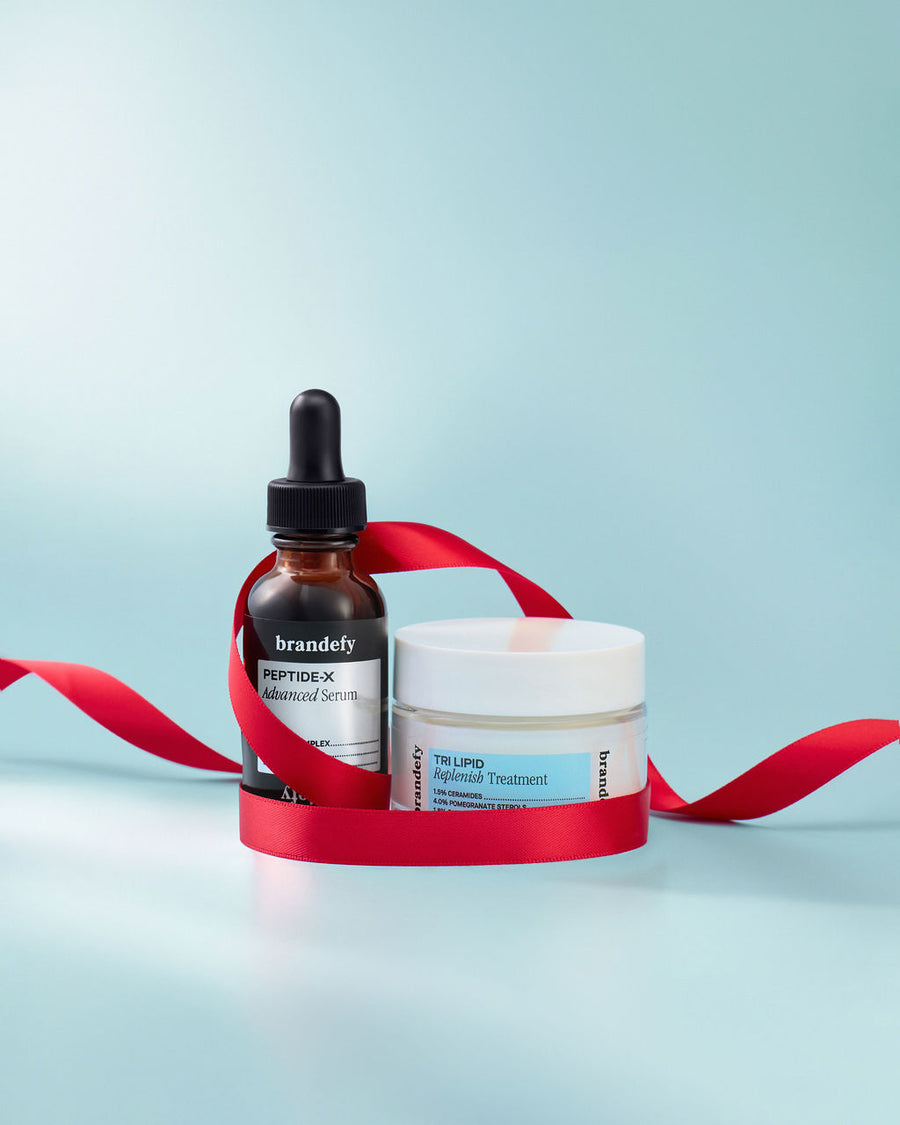 The Peptide-X Advanced Serum bottle and the Tri Lipid Replenish Treatment jar together on a pale blue ground, with a red satin ribbon looped around them.