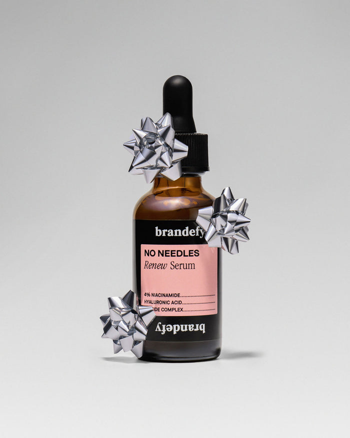 The No Needles Renew Serum bottle on a pale blue ground, decorated with silver gift bows.