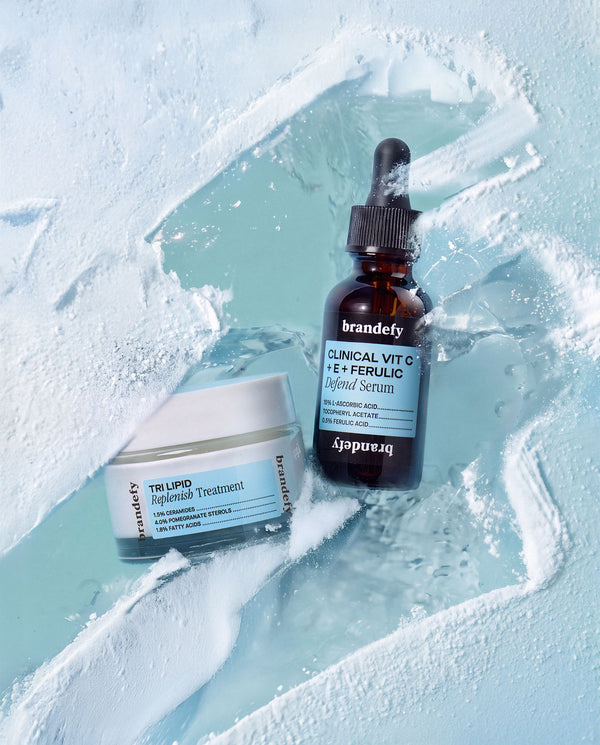 The Clinical Vit C + E + Ferulic serum and the Tri Lipid Replenish Treatment jar resting on cracked ice and snow.