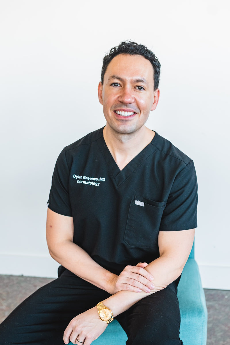 Dr. Dylan Greeney, board-certified dermatologist and Brandefy partner, seated in black scrubs.